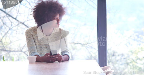 Image of black woman drinking coffee and using a mobile phone  at home