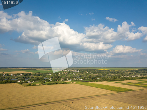 Image of Summer countryside landscape with agricultural fields with crops and after harvesting on a background of blue cloudy sky.