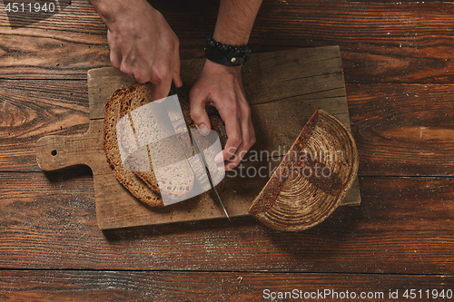 Image of Hands of young man cut dark bread