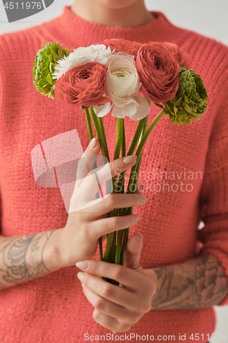 Image of Young girl in a sweater in a color of the year 2019 Living Coral Pantone holding a bouquet of fresh flowers in her hands with tatoo.