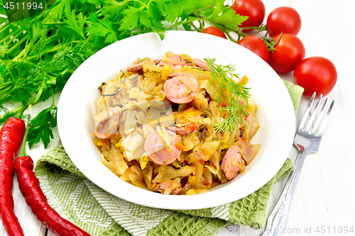 Image of Cabbage stew with sausages in white plate on napkin