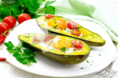 Image of Scrambled eggs with tomatoes in avocado on light wooden board