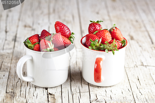 Image of Organic red strawberries in two white ceramic cups on rustic woo