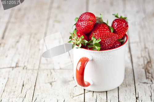 Image of Organic red strawberries in white ceramic cup on rustic wooden b