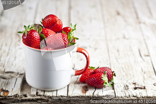 Image of Organic red strawberries in white ceramic cup on rustic wooden b