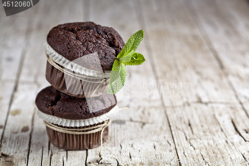 Image of Chocolate dark muffins with mint leaves on rustic wooden table.