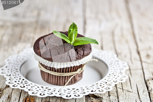 Image of Fresh dark chocolate muffin with mint leaves on white plate on r
