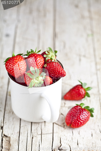 Image of Organic red strawberries in white ceramic cup on rustic wooden b