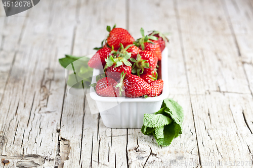 Image of Fresh red strawberries in white bowl and mint leaves on rustic w