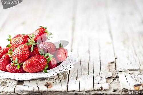 Image of Red strawberries on white plate on rustic wooden background.
