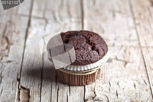 Image of Fresh single dark chocolate muffin on rustic wooden table.