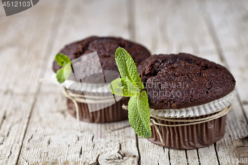 Image of Chocolate dark muffins with mint leaves closeup on rustic wooden