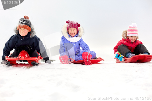 Image of happy little kids sliding down on sleds in winter