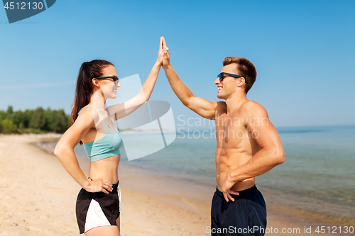 Image of happy couple in sports clothes and shades on beach