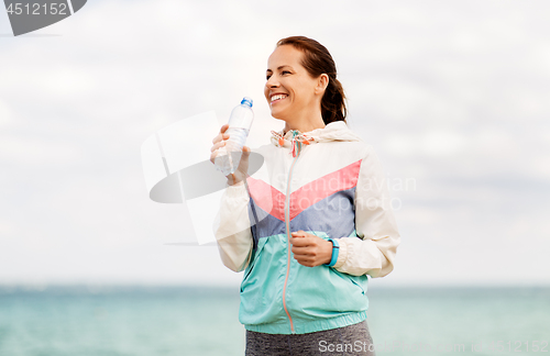Image of woman drinking water after exercising at seaside