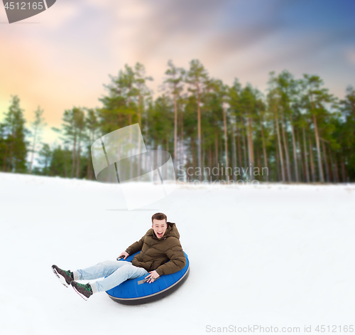 Image of happy young man sliding down hill on snow tube