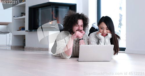 Image of young multiethnic couple using a laptop on the floor