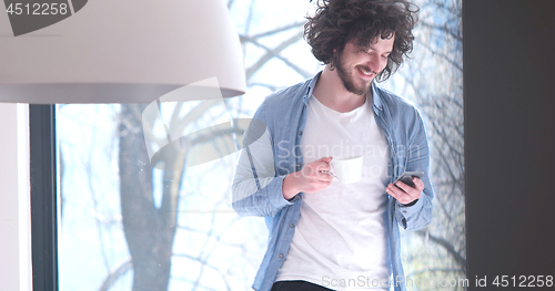 Image of young man drinking coffee and using a mobile phone  at home