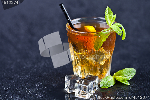 Image of Iced tea with lemon, mint leaves and ice cubes in glass on wet b