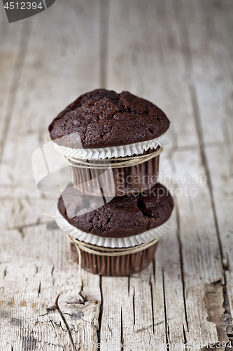 Image of Two dark chocolate dark muffins on rustic wooden table.