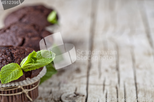 Image of Chocolate dark muffins with mint leaves closeup on rustic wooden