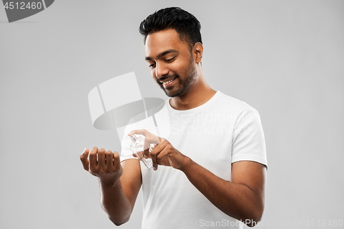 Image of happy indian man with perfume over gray background