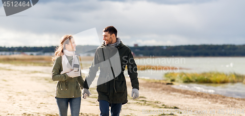 Image of couple with tumbler walking along autumn beach