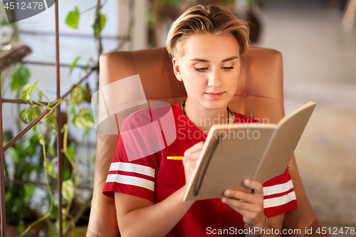 Image of teenage girl writing to notebook at cafe