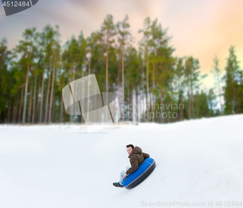 Image of happy young man sliding down hill on snow tube
