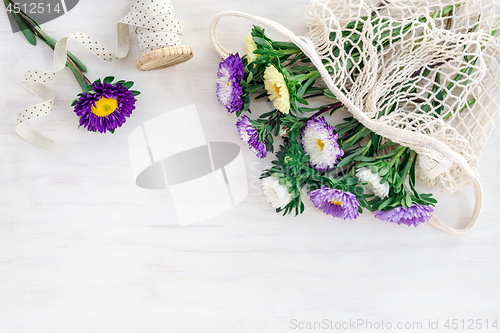 Image of Asters in a mesh bag on white wooden background
