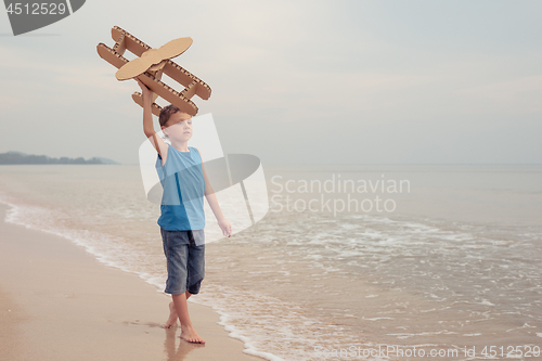 Image of Little boy playing with cardboard toy airplane on the beach