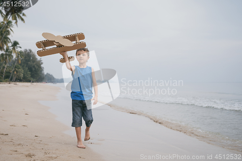 Image of Little boy playing with cardboard toy airplane on the beach