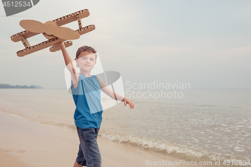 Image of Little boy playing with cardboard toy airplane on the beach