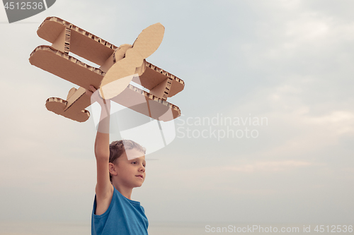 Image of Little boy playing with cardboard toy airplane on the beach