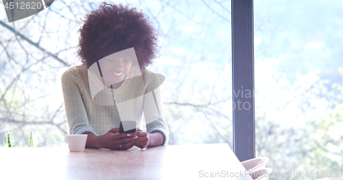 Image of black woman drinking coffee and using a mobile phone  at home