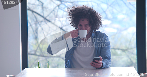 Image of young man drinking coffee and using a mobile phone  at home