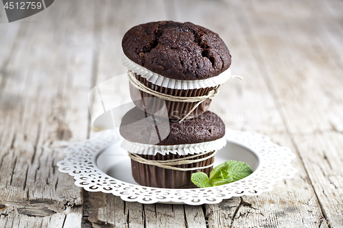 Image of Two fresh dark chocolate muffins with mint leaves on white plate