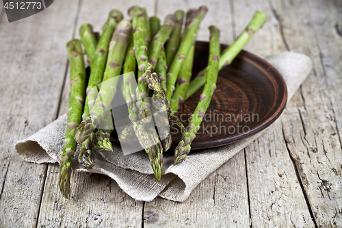 Image of Fresh raw garden asparagus closeup on brown ceramic plate and li