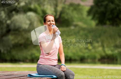 Image of woman drinking water after exercising in park