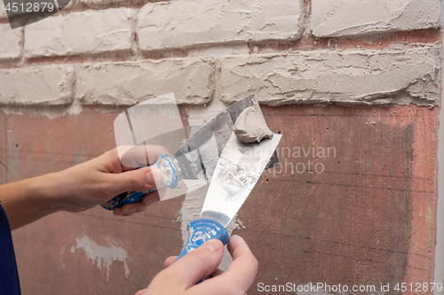 Image of Plasterer works with two spatulas applying plaster on the wall