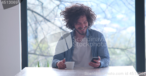 Image of young man drinking coffee and using a mobile phone  at home