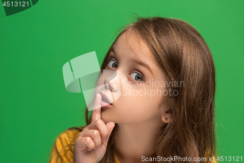 Image of The young teen girl whispering a secret behind her hand over green background