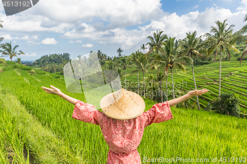 Image of Relaxed fashionable caucasian woman wearing red asian style kimono and traditional asian paddy hat, arms rised to sky, enjoying pure nature at beautiful green rice fields on Bali island