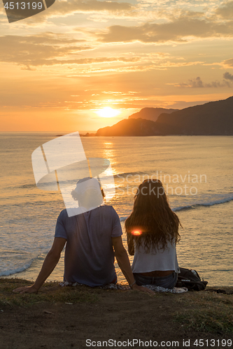 Image of Romantic couple on vacation sitting and watching colorful sunset over the sea coast.