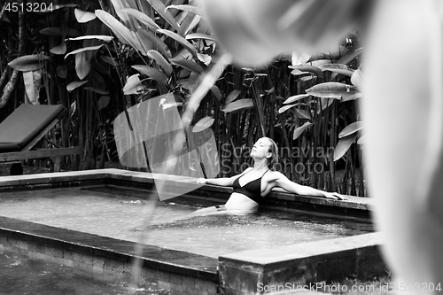 Image of Sensual young woman relaxing in outdoor spa infinity swimming pool surrounded with lush tropical greenery of Ubud, Bali. Black and white image.