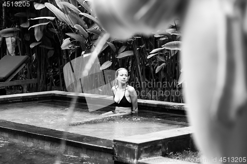 Image of Sensual young woman relaxing in outdoor spa infinity swimming pool surrounded with lush tropical greenery of Ubud, Bali. Black and white image.