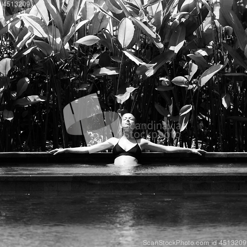 Image of Sensual young woman relaxing in outdoor spa infinity swimming pool surrounded with lush tropical greenery of Ubud, Bali. Black and white image.