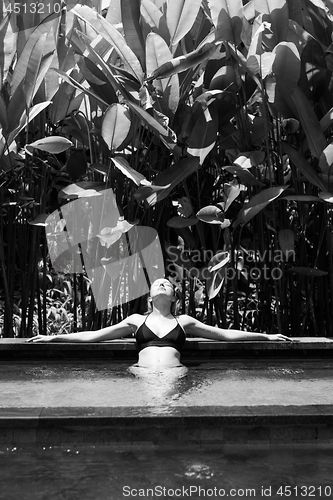 Image of Sensual young woman relaxing in outdoor spa infinity swimming pool surrounded with lush tropical greenery of Ubud, Bali. Black and white image.