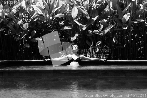 Image of Sensual young woman relaxing in outdoor spa infinity swimming pool surrounded with lush tropical greenery of Ubud, Bali. Black and white image.