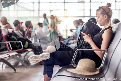 Image of Female traveler using her cell phone while waiting to board a plane at departure gates at asian airport terminal.